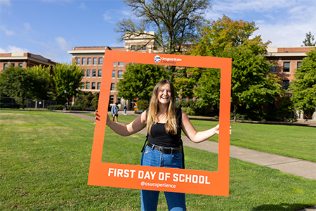 A student holds a giant orange frame making it look like they are in a giant polaroid photo.