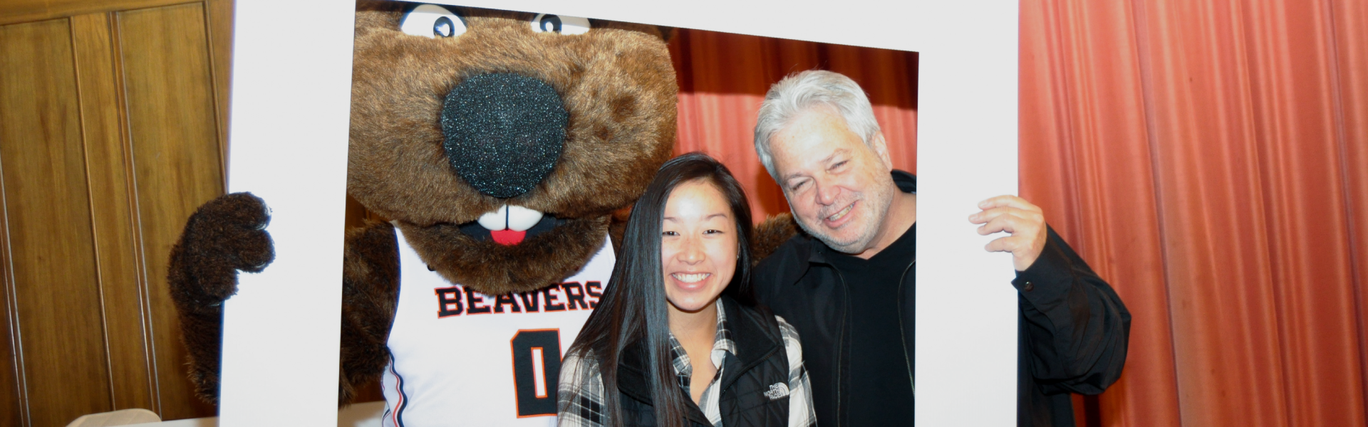 Beaver family members, including father and daughter, taking a photo with Benny at OSU