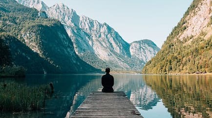 Person sitting on a dock by a lake with mountains