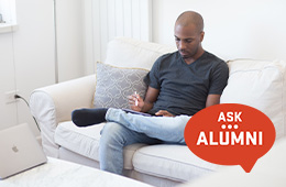 Person sitting on a white couch using a laptop and writing on a tablet. Graphic overlay reads "Ask Alumni."