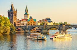 Charles Bridge in Prague with river boats on the river at sunset