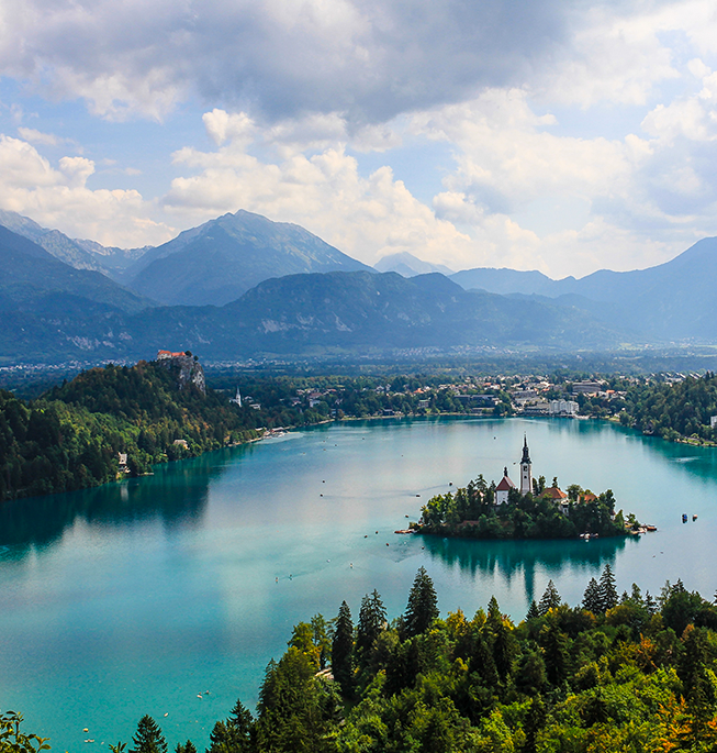 Landscape of Lake Bled with an island in the middle which has buildings, background includes more mountains