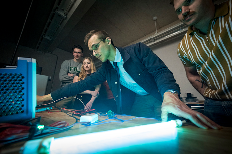 A group of four people working at a table with technical equipment and a glowing blue light in a dimly lit room.
