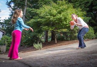 mother and daughter throwing a children's basketball back and forth outside