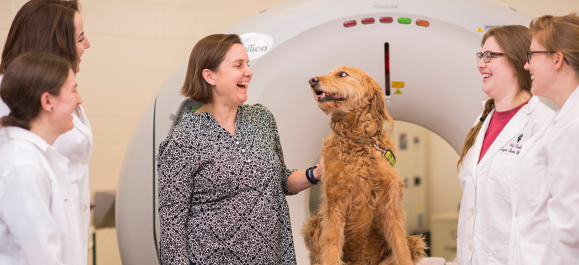 Dr. Stieger Vanegas with her dog at an MRI machine with 4 students in white lab coats.