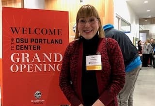 Professor of Art Emerita Kay Campbell at the OSU Portland Center next to sign that reads 