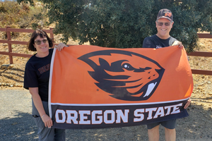 Sue is pictured with her husband Randy, holding a flag with OSU Beaver logo with text 