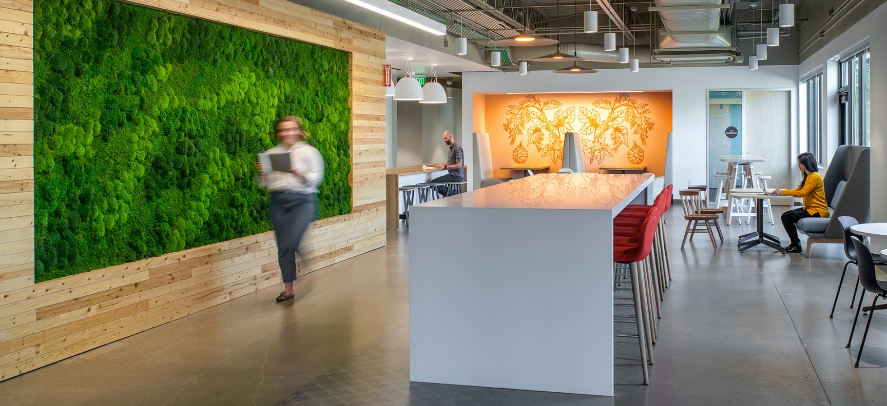 Entry area of Research Way. There is a bright green moss wall on the left with tables and chairs filling up the right side.