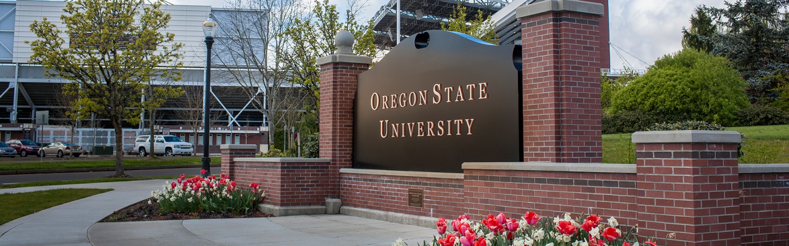 The Oregon State University sign surrounded by a brick structure with flower beds below