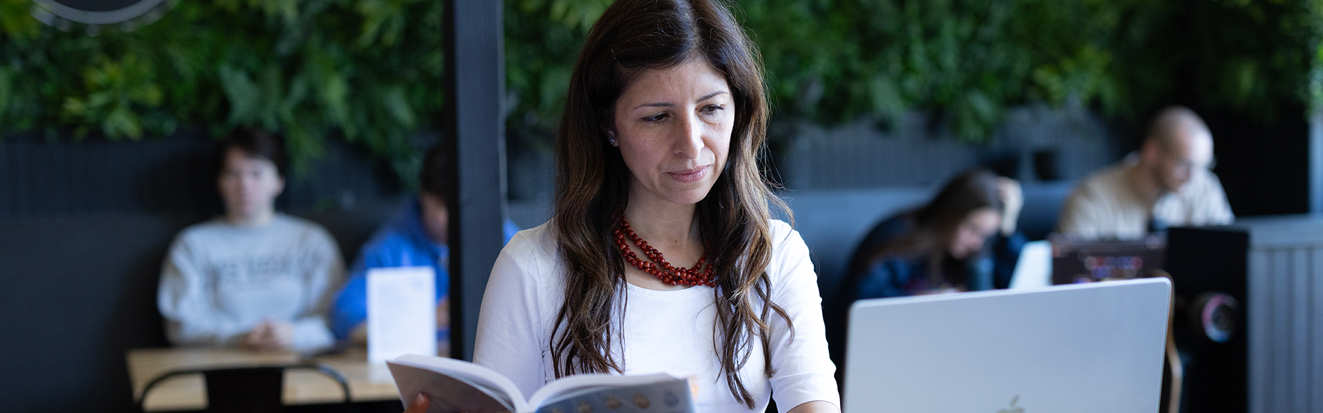 A person with an open book and laptop in a public outdoor setting.