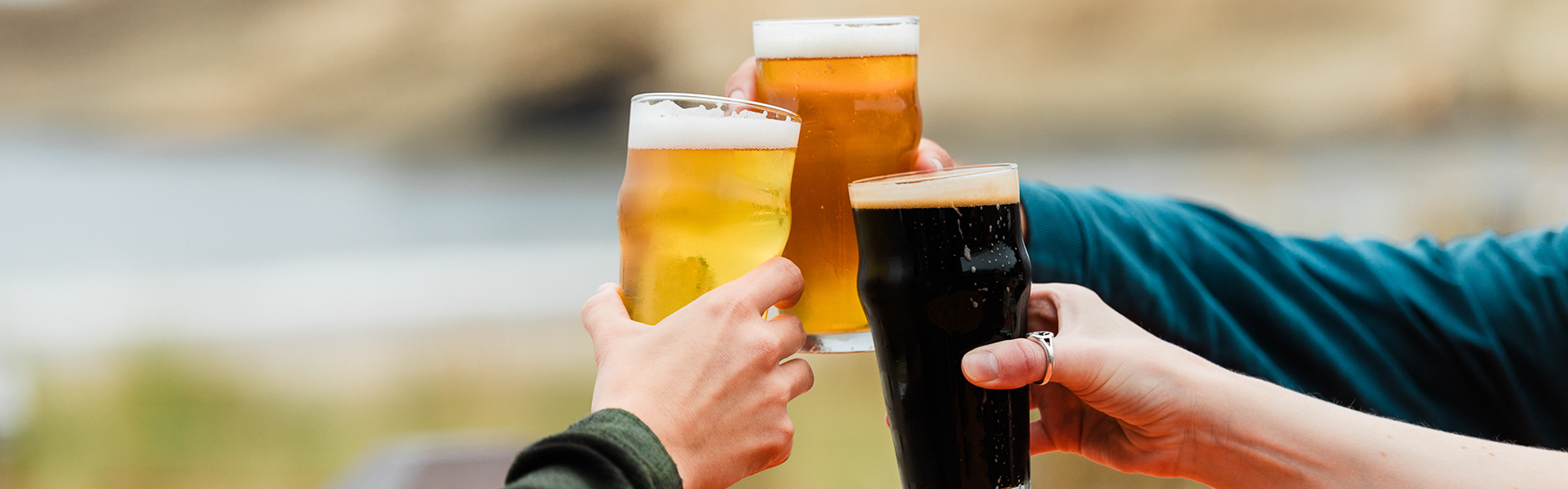 People toast with glasses of beer at a beachside gathering.
