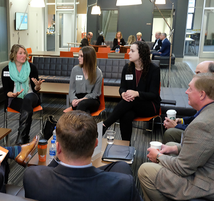 A group of nine people in business attire. One speaks while the others listen.