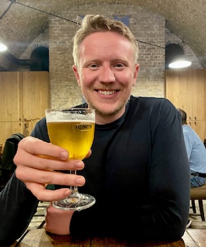 Person seated at a wooden table in a restaurant, holding a glass of beer.