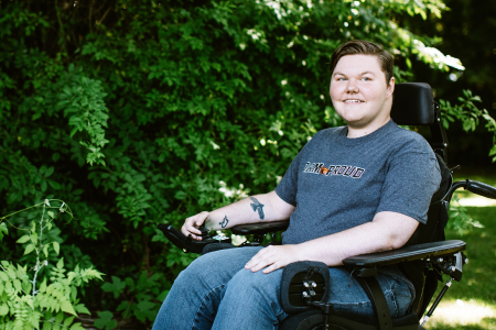 Kolbey Bonin in his wheelchair surrounded by beautiful greenery and dappled light.