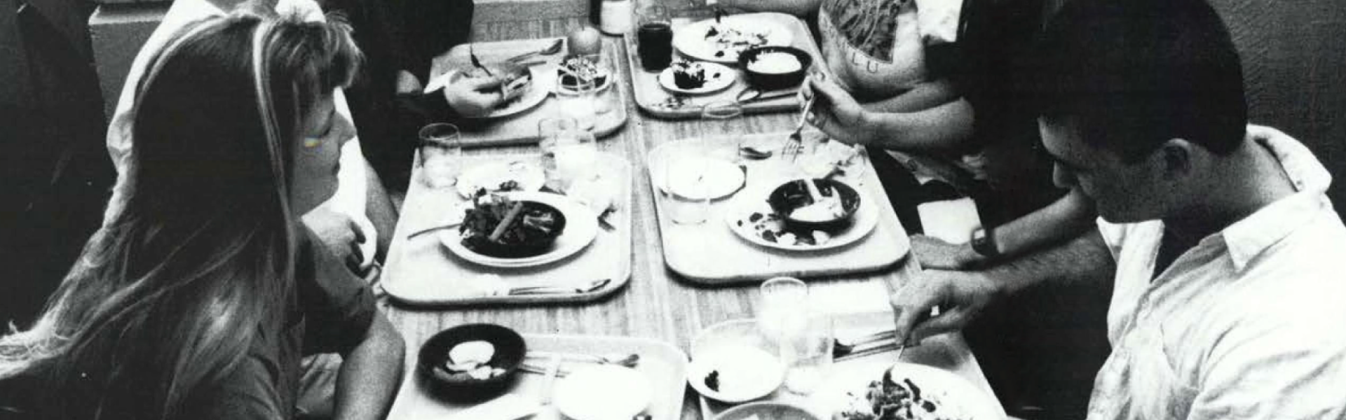 Black and white photo taken in 1992 of students with lunch trays eating at a lunch table