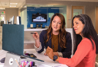 Two female coworkers discussing something that is on a computer.
